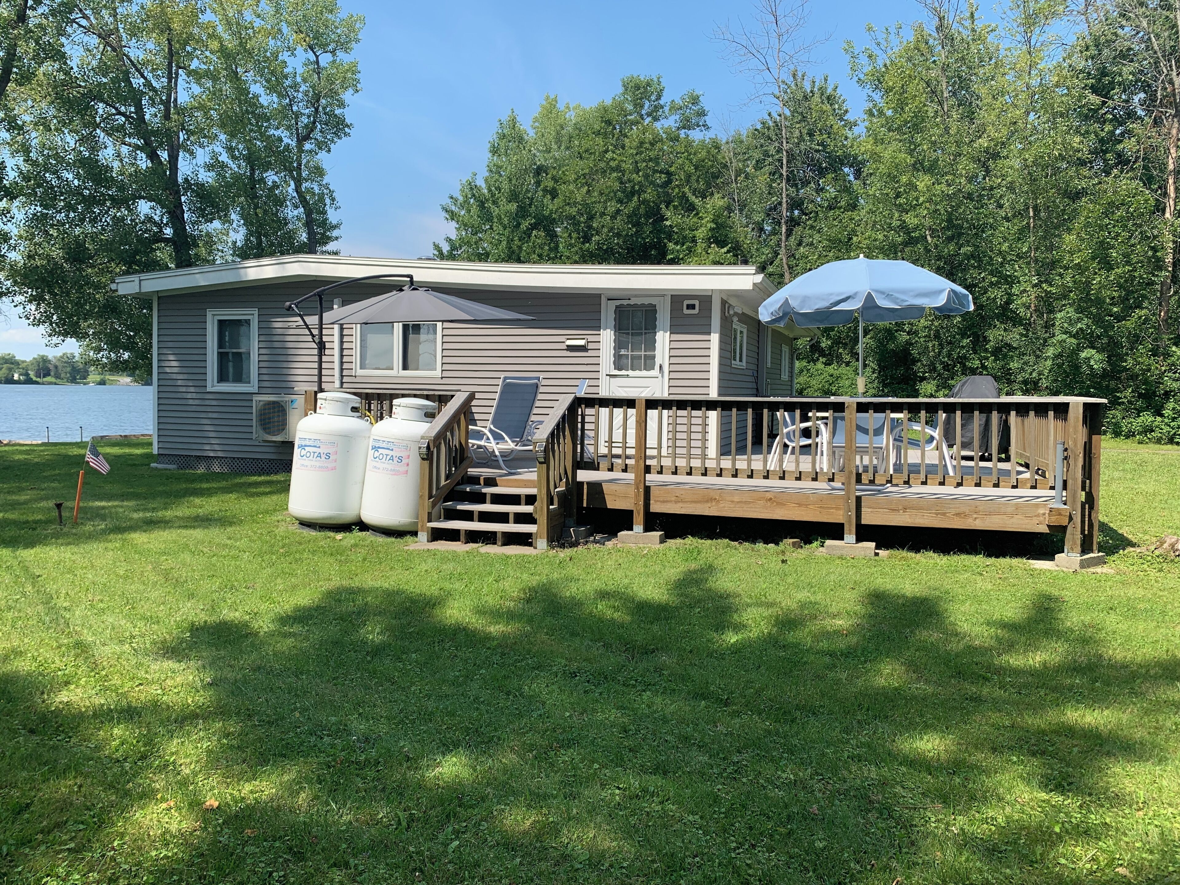 A small cabin with a deck, outdoor seating, and propane tanks.