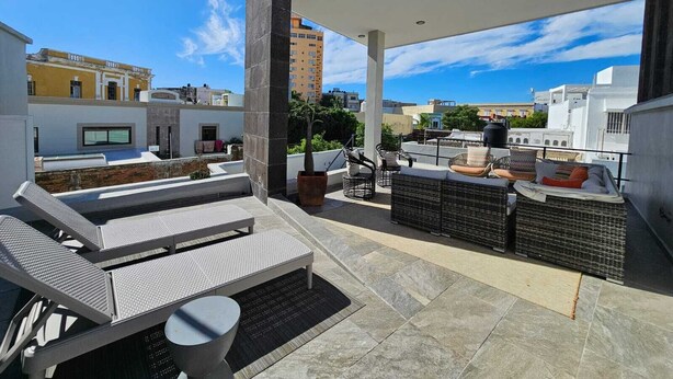 A rooftop terrace with outdoor seating, a potted plant, and a view of the cityscape.