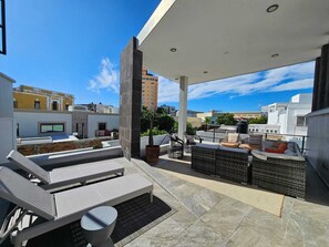 Una terraza en la azotea con mobiliario exterior, una planta en maceta y vistas de la ciudad.