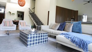 A modern living room with a sofa, armchairs, a coffee table, and a staircase leading to a kitchen.