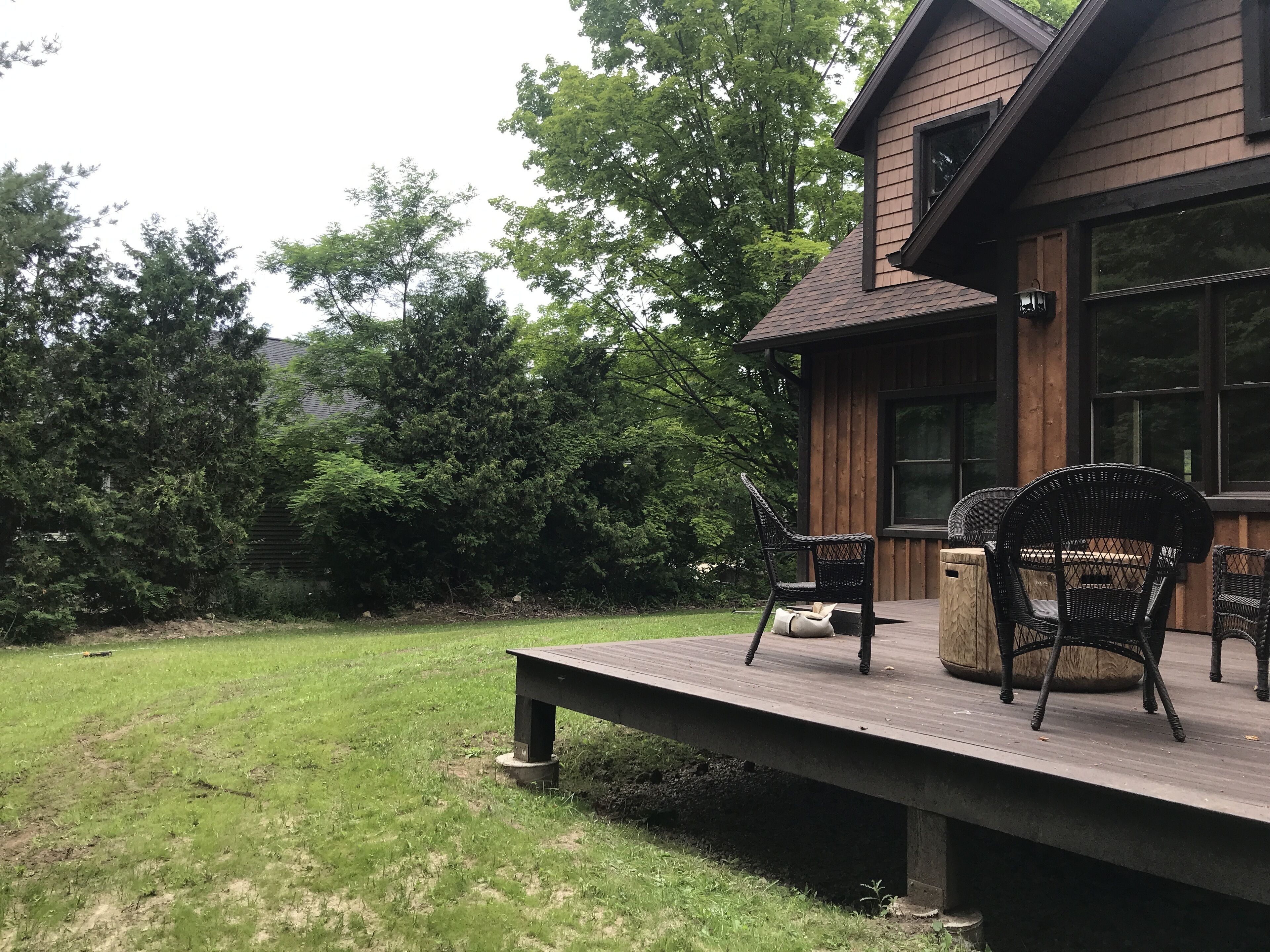 A wooden deck with outdoor furniture, surrounded by a grassy lawn and dense trees.