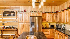 A wooden cabin-style kitchen with a central island, wooden cabinets, and a stainless steel refrigerator. -  Larsen Lodge Downtown Village Egg Harbor, Sauna, New, Rustic and Elegant. (Egg Harbor)