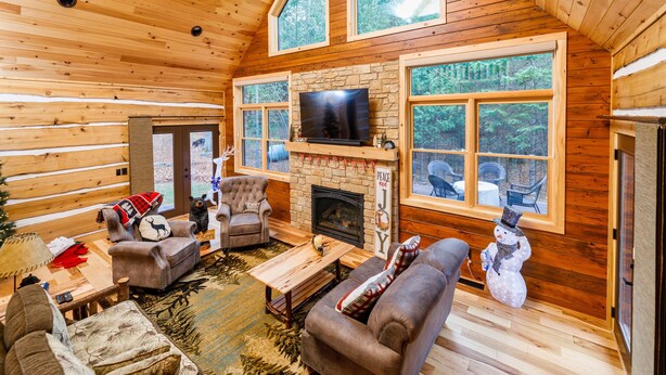 A cozy cabin interior with a stone fireplace, wooden walls, and large windows offering a view of the forest. -  Larsen Lodge Downtown Village Egg Harbor, Sauna, New, Rustic and Elegant. (Egg Harbor)