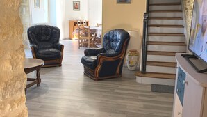 A living room with two leather armchairs, a dining area with wooden furniture, a staircase, and a television on a cabinet. - Listed country house in Périgord between Sarlat, Lascaux and Rocamadour (Salignac-Eyvigues)
