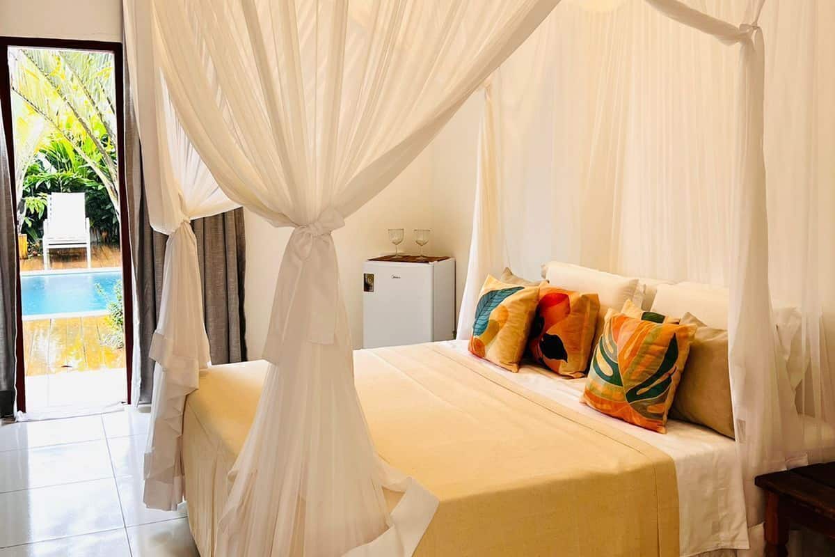Un dormitorio con cama a dosel, una mesita con dos vasos y vista a una piscina por una puerta abierta.