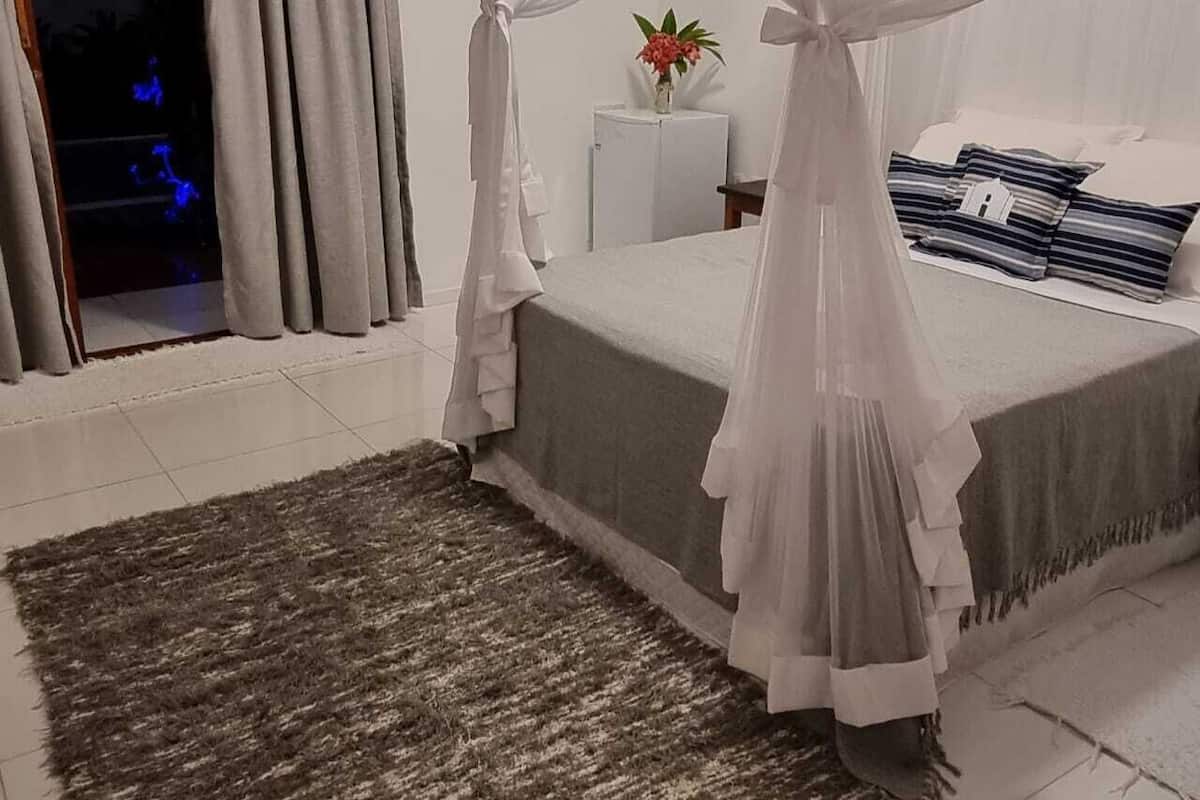 Un dormitorio con cama, mesita de noche, una pequeña mesa con un florero y una ventana con cortinas.