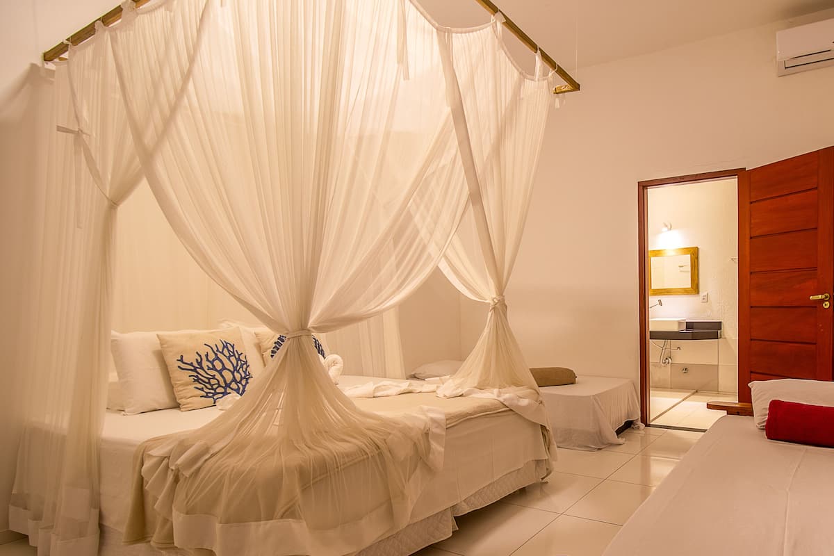Un dormitorio con cama a dosel, una mesita de noche pequeña y un cojín rojo.