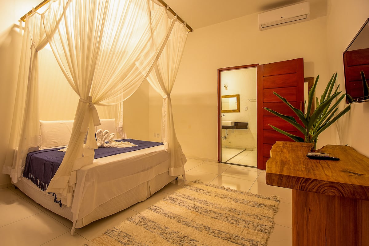 Un dormitorio con cama con dosel, una mesita de noche de madera y una puerta roja que da al baño.