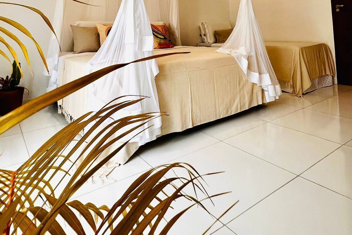 Un dormitorio con cama con dosel, una planta en maceta y suelo de baldosas.