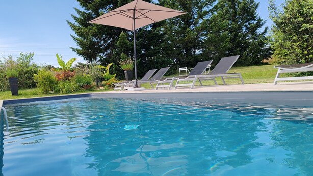 A clear swimming pool with lounge chairs and an umbrella.
