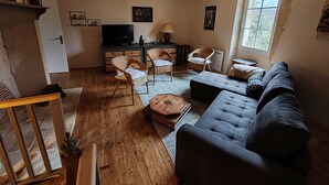 A cozy living room with a sofa, wicker chairs, a TV, and a chandelier.