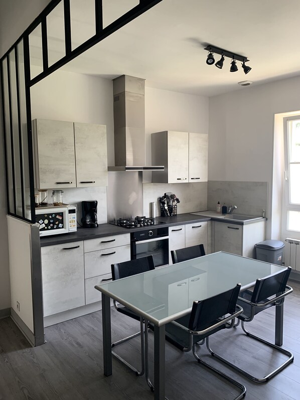 A modern kitchen with white cabinets, a glass dining table, and black chairs. - Charming townhouse with a garden (Pons)