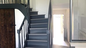 Un escalier moderne avec des rampes noires et des marches en bois, menant à un couloir lumineux.