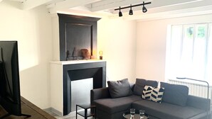 Un salon moderne avec un canapé gris, une petite table d’appoint, un téléviseur posé sur un meuble en bois et une cheminée.