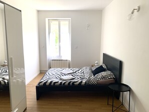 Un dormitorio con cama, mesita de noche, radiador y ventana.