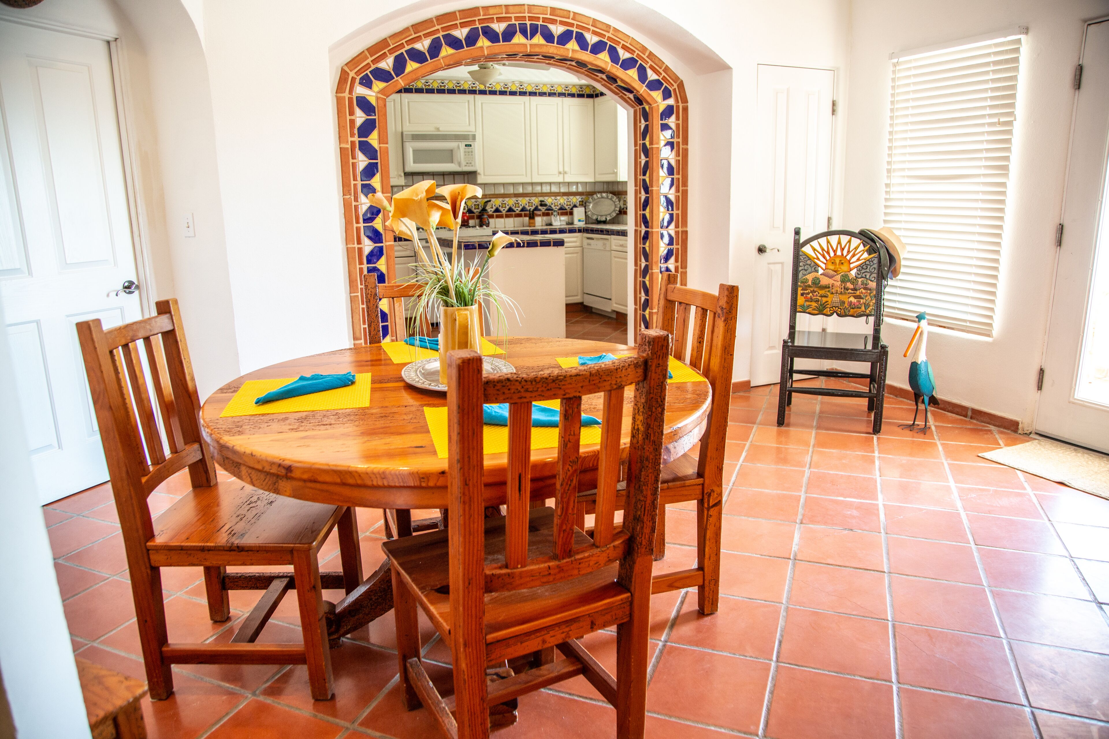 A dining area with a wooden table and chairs, a tiled backsplash, and a view of the kitchen.