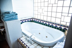 A bathroom with a white bathtub, tiled walls, and a window with blinds.