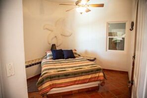 A bedroom with a bed, a ceiling fan, a starfish decoration, and a window.