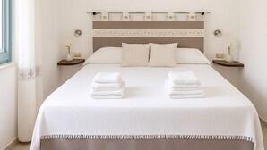 A hotel room with a large bed, two bedside tables, an air conditioning unit above the bed, and a window with curtains. - Panoramic Villa Sea View  (Quartu Sant'Elena)