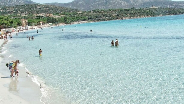 A beach with clear water, people swimming, and a distant shoreline with buildings. - Panoramic Villa Sea View  (Quartu Sant'Elena)