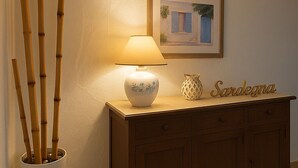 A lamp on a wooden cabinet, a framed picture on the wall, and a bamboo plant in a white pot. - Panoramic Villa Sea View  (Quartu Sant'Elena)