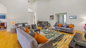 Un salon spacieux avec un canapé gris, des coussins orange, une table basse et une moto en arrière-plan.