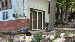 A garden with various potted plants and rocks, a wheelbarrow, and a house with a brick facade and a sliding glass door. - Great location 2 minutes Walking to downtown and to the lake (Fish Creek)