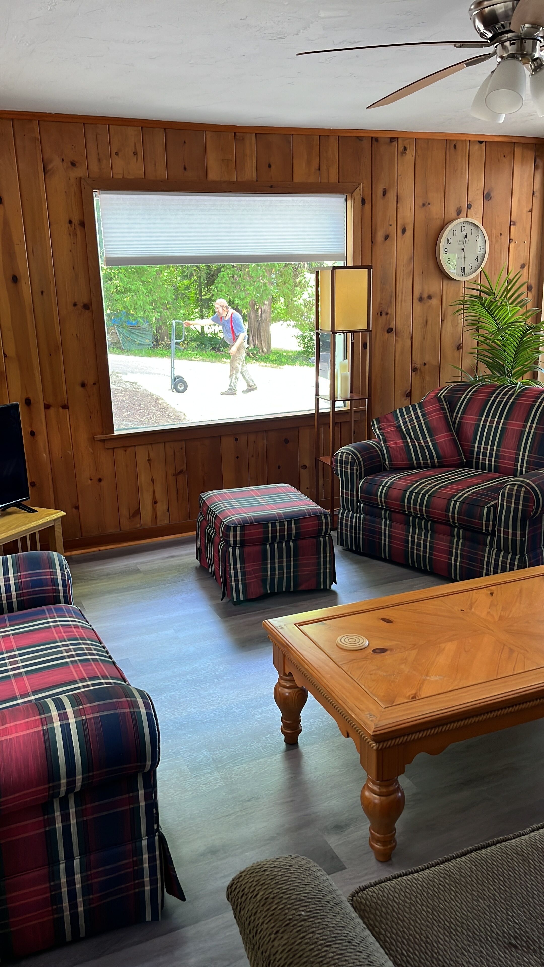 Una sala de estar acogedora con muebles de cuadros, techo de madera y un amplio ventanal con vistas a una entrada de vehículos.