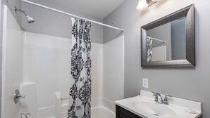 Un bany modern amb dutxa, un mirall gran i un lavabo blanc.
