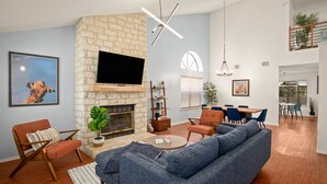 Ein modernes Wohnzimmer mit Kamin aus Stein, einem Flachbildfernseher, einer Couch und einem Essbereich mit Stühlen und Tisch.