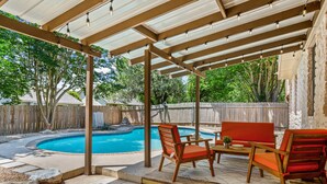 Eine überdachte Terrasse mit Pool, Holzstühlen und einem Tisch.