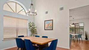 Ein Essbereich mit einem Holztisch, blauen Stühlen, einem Blumentopf und einem gerahmten Bild an der Wand.