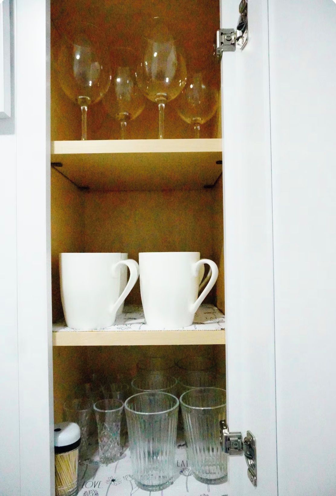 A cabinet with shelves holding wine glasses, white cups, and clear glasses.