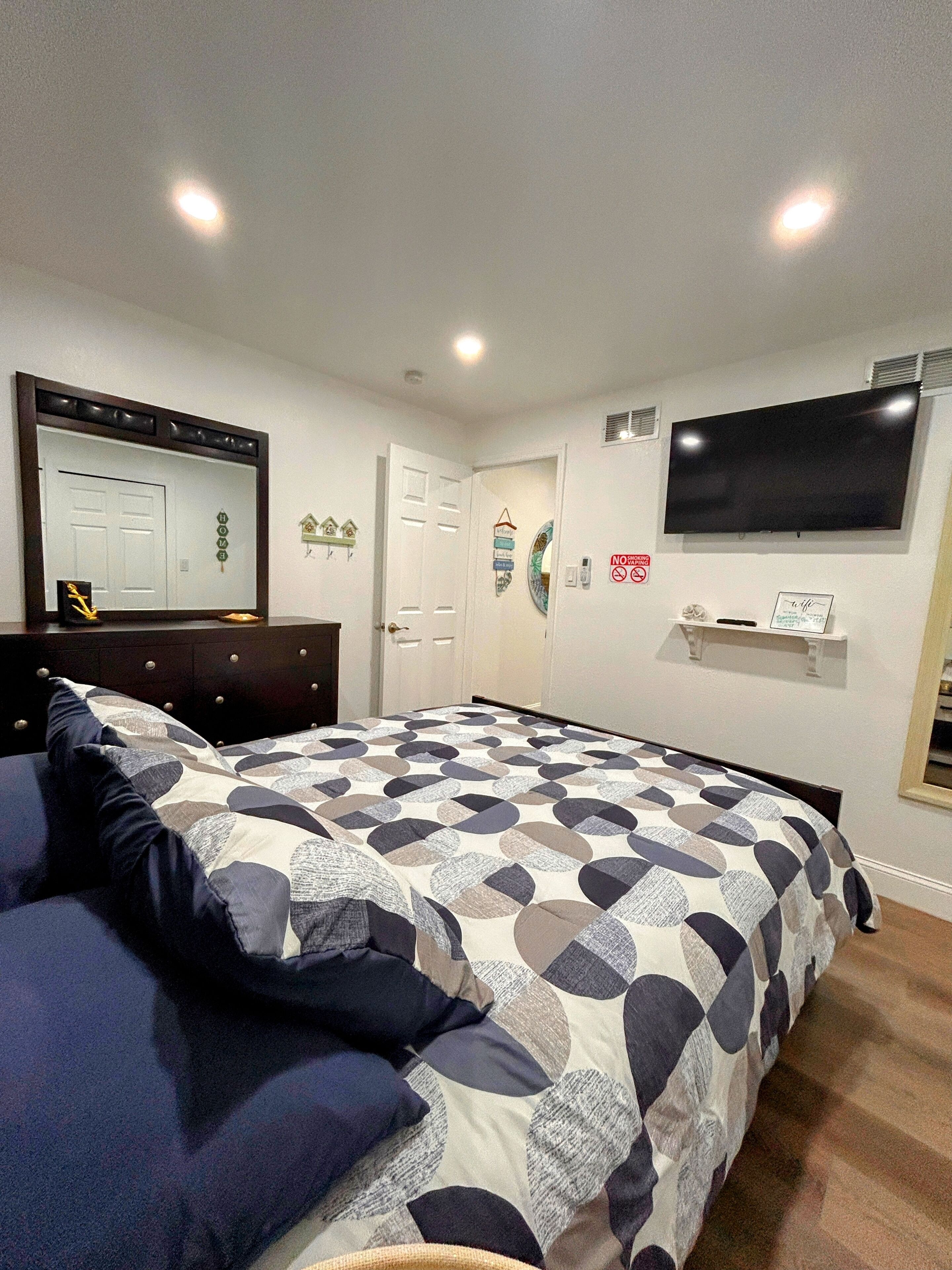 A bedroom with a bed, dresser, mirror, TV, and a door.