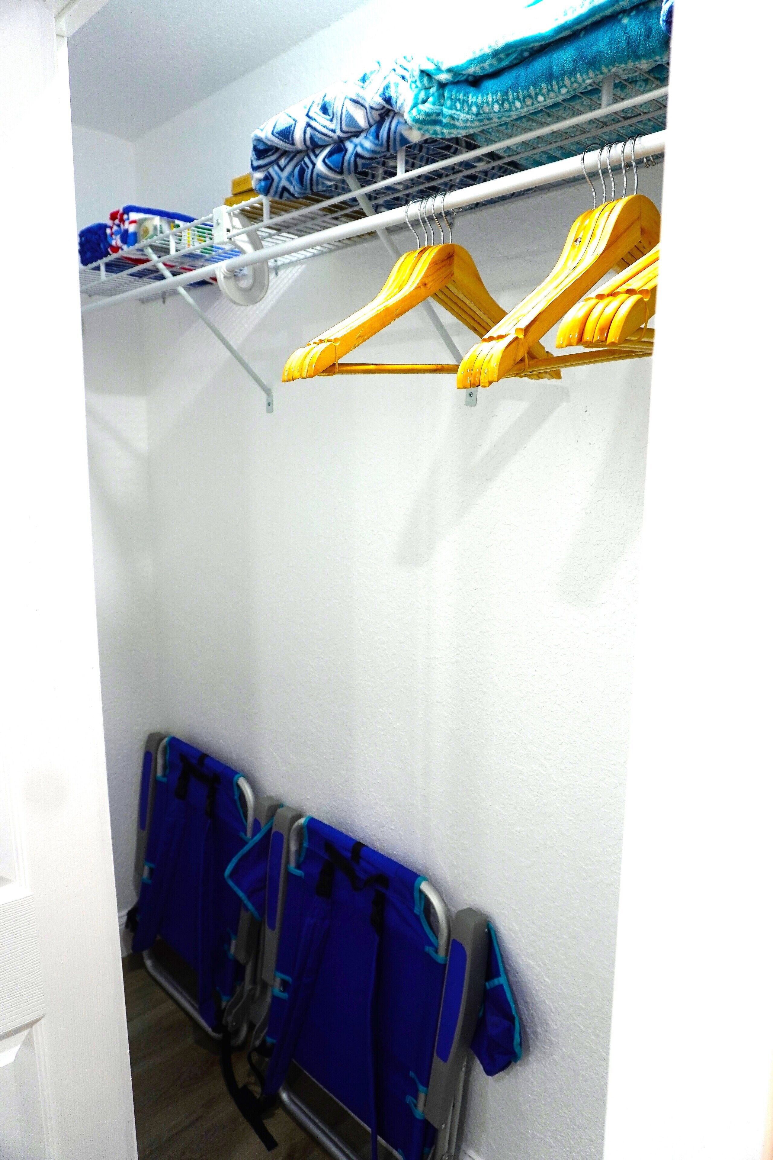 Armário com prateleiras e cabides para roupas, e um suporte com sacolas azuis.