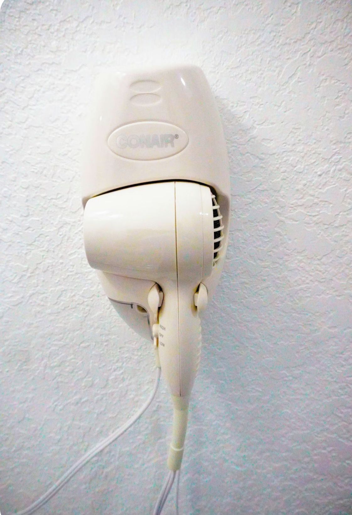Ein weißer Haartrockner an einer strukturierten Wand befestigt.