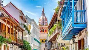 A narrow street with buildings on either side, a prominent church spire in the distance, and a blue building on the right. - 2CL1-J Apartamento en el Centro Histórico (Cartagena)