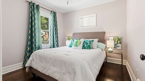Een slaapkamer met een bed, een nachtkastje, een raam met gordijnen en een wandlamp.