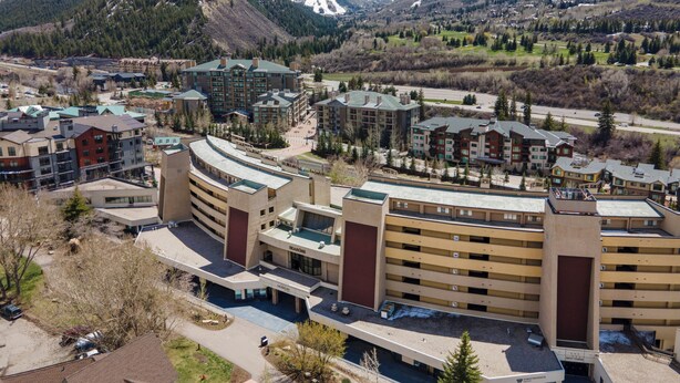A modern hotel complex with multiple buildings, a parking garage, and a view of snow-capped mountains in the background. - Modern Condo in Avon, Walk to BC Gondola, SA228 (Avon)
