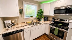 A modern kitchen with white cabinets, stainless steel appliances, a dishwasher, and a window with blinds.