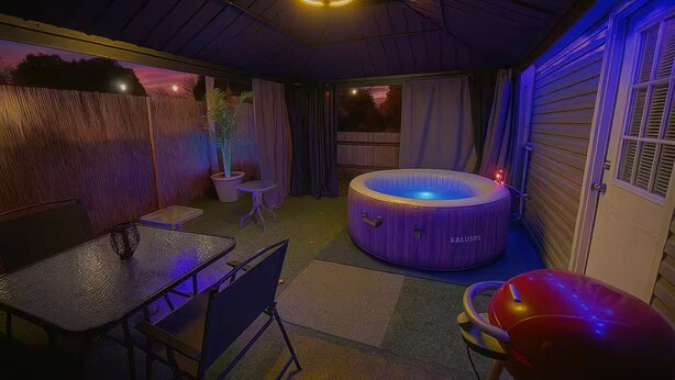 Un jacuzzi en un espacio exterior cubierto con una mesa y sillas, rodeado por un muro de madera y una ventana.