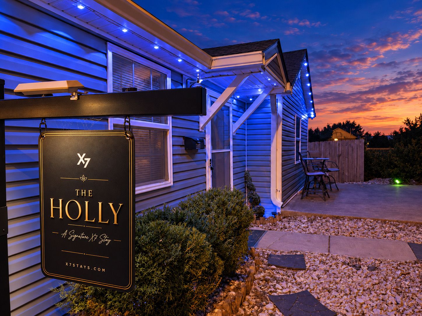 A sign for 'The Holly' hotel with a website address, a covered outdoor seating area, and a sunset in the background.