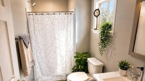 Un baño con ducha, inodoro, lavamanos y una pequeña planta en maceta.