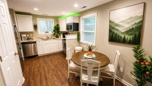 Una cocina moderna con armarios blancos, electrodomésticos de acero inoxidable y un comedor con mesa redonda de madera y sillas blancas.
