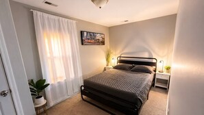 Un dormitorio con una cama, mesitas de noche, una planta en maceta y un cuadro en la pared.