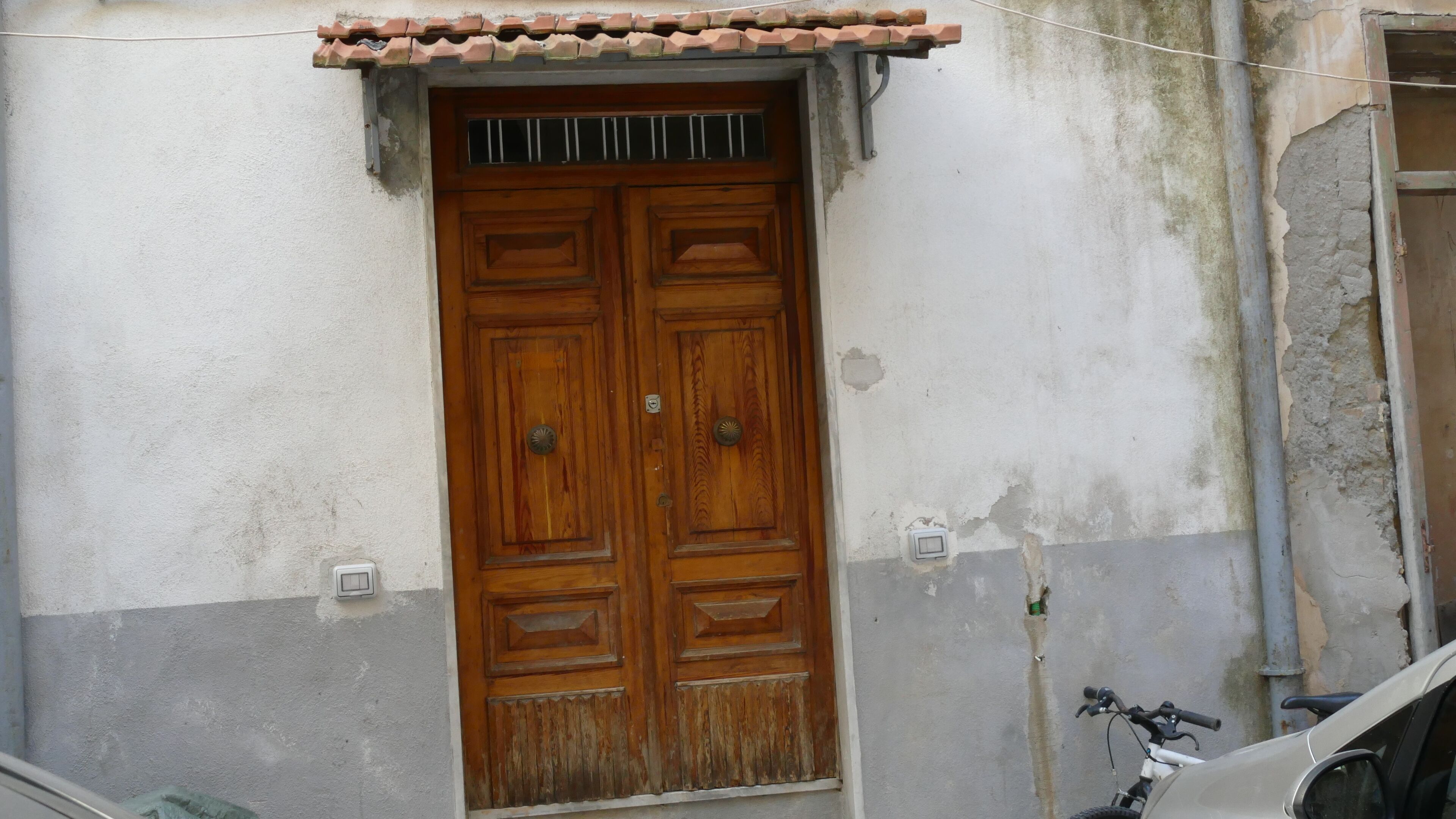 A wooden double door with a metal handle, set in a building with a grey and white exterior.