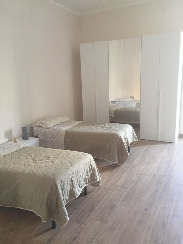 A bedroom with two beds, a wardrobe, and a bedside table.