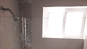 A glass-enclosed shower with patterned tiles and a small window at the top.