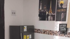 A compact kitchen with a refrigerator, a dining table with chairs, and a tiled backsplash.