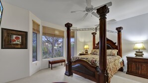 A four-poster bed with a canopy, a wooden nightstand with a lamp, a bench, and a framed picture on the wall.